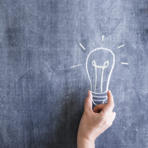 person-holding-light-bulb-drawn-chalkboard
